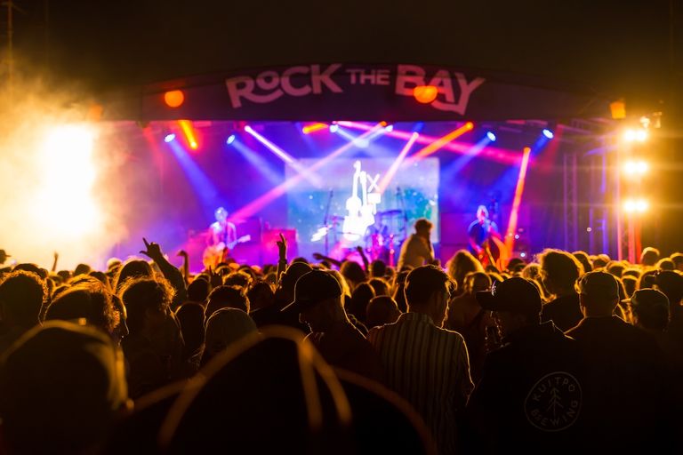 Crowd watching a live band perform on stage under bright concert lights at the Rock the Bay music festival.